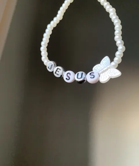 A pearl bead bracelet with a white butterfly charm and letter beads spelling JESUS.
