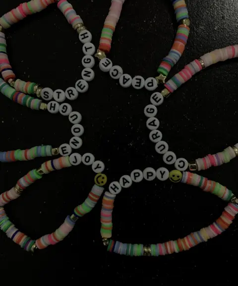 Five clay disc bead bracelets spelling STRENGTH, ENOUGH, JOY, PEACE, HAPPY and COURAGE, laid out on black.