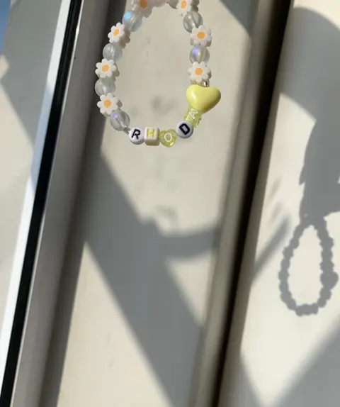 A bracelet of daisy beads, frosted beads and a yellow heart, with letter beads spelling RHODA.