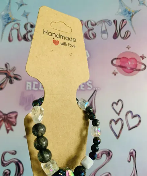 A bracelet of dark crackled glass beads, clear faceted crystals and an iridescent heart on a Handmade with love card.