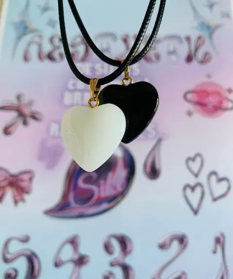 A white heart pendant and a black heart pendant on black cords.