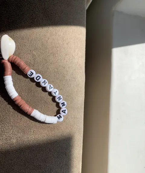 A clay disc bracelet in terracotta and white with a cowrie shell, spelling MAMTANDE.
